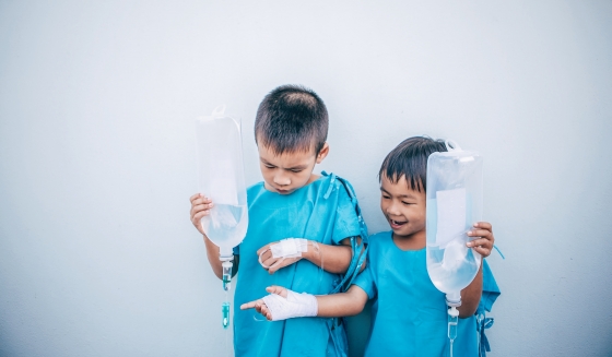 Two young boys wearing blue hospital gowns playing outside