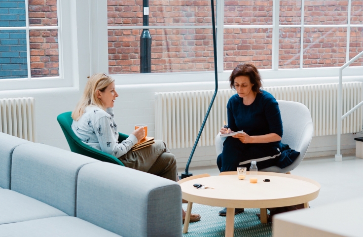 Two women sitting on a couch in a stylish office discussing work